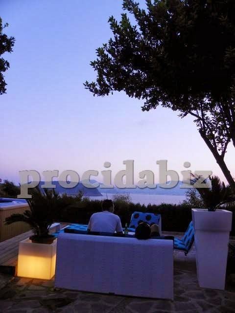 Twilight view of a waterfront terrace with illuminated seating area and sea vista at dusk.