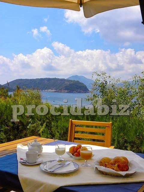 Breakfast table with sea view overlooking a Mediterranean bay with islands and mountains in the distance.